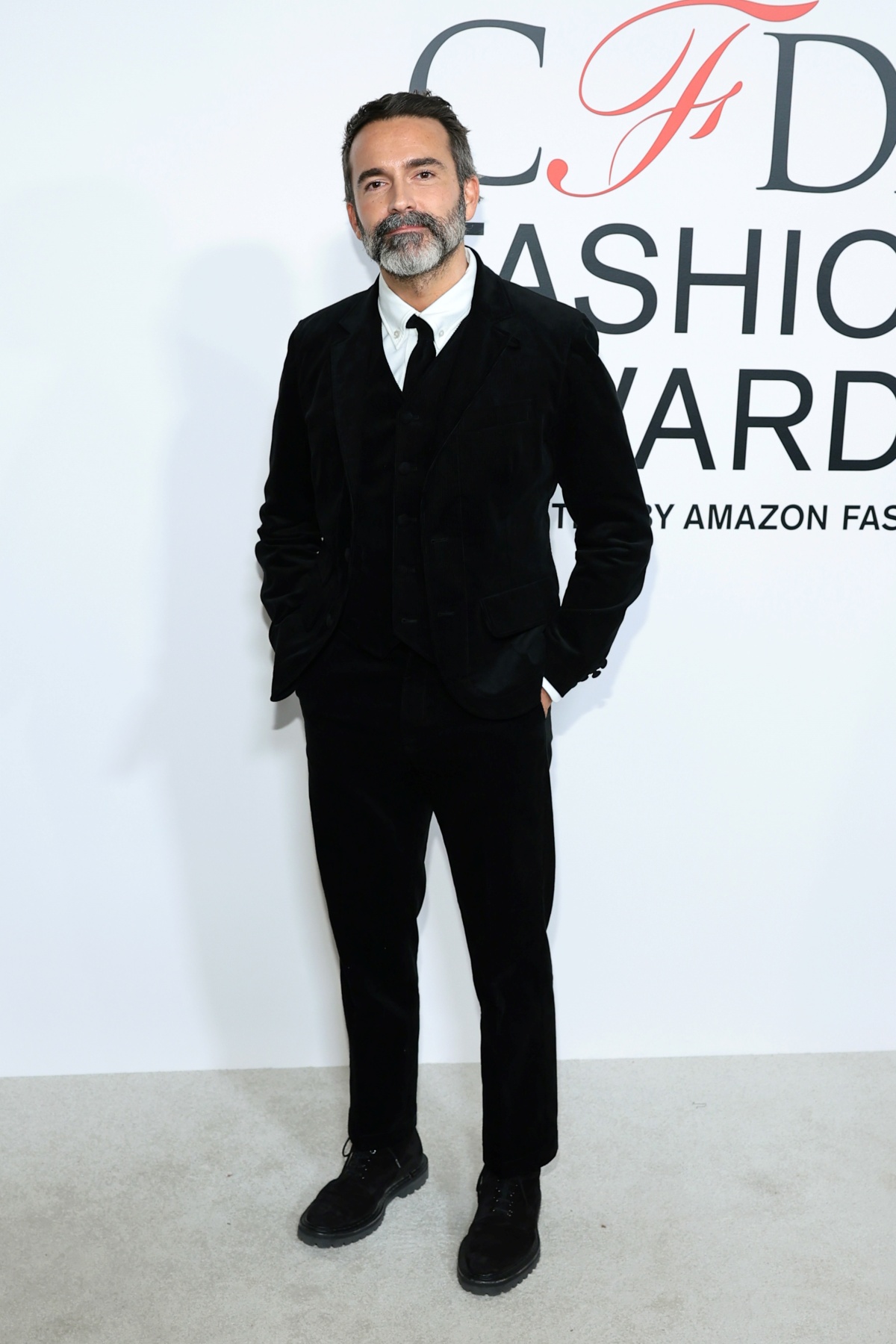 A imagem mostra o designer Daniel Roseberry vestindo um terno preto em frente ao backdrop com a logo do CFDA Fashion Awards 2024