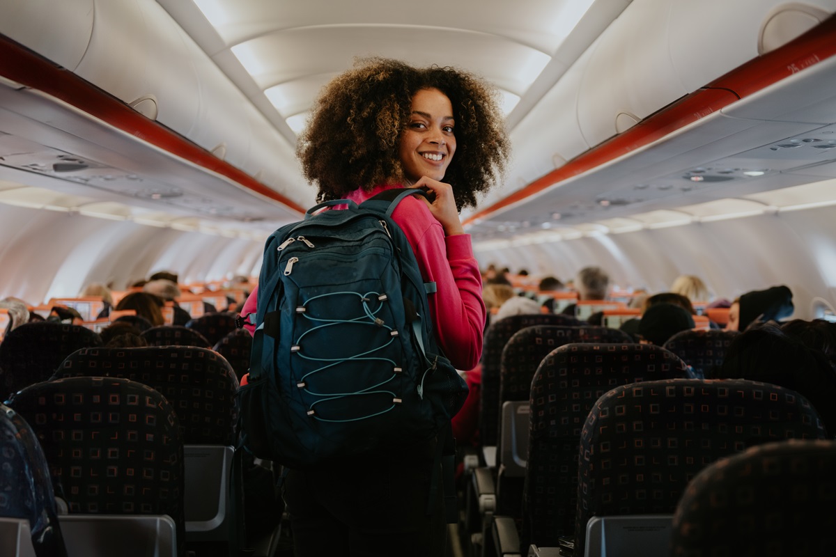 foto colorida - mulher negra com blusa rosa e mochila nas costas no avião 