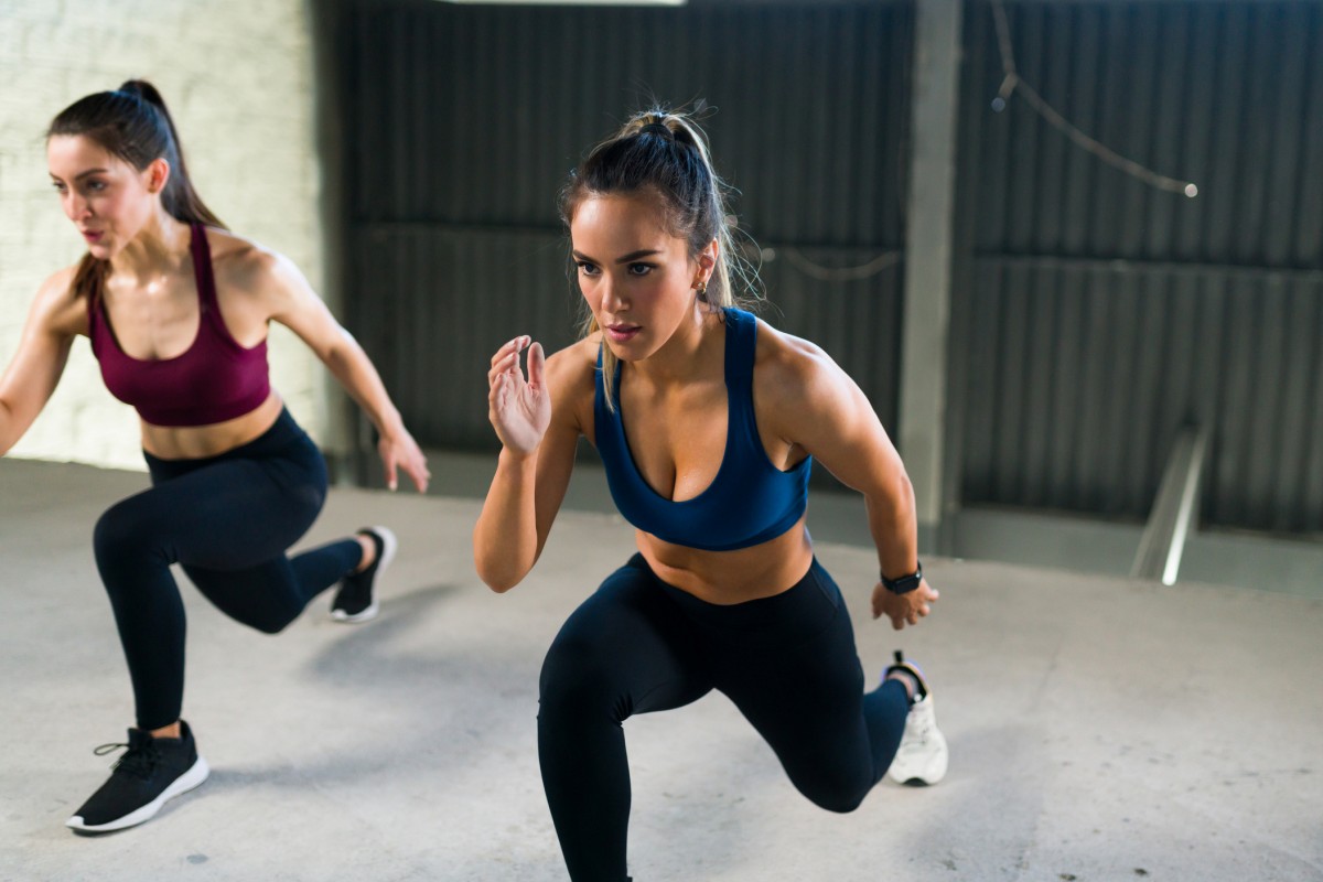 Jovem atlética com um estilo de vida saudável fazendo estocadas nas pernas durante uma aula de HIIT. Mulheres malhando juntas na academia de ginástica