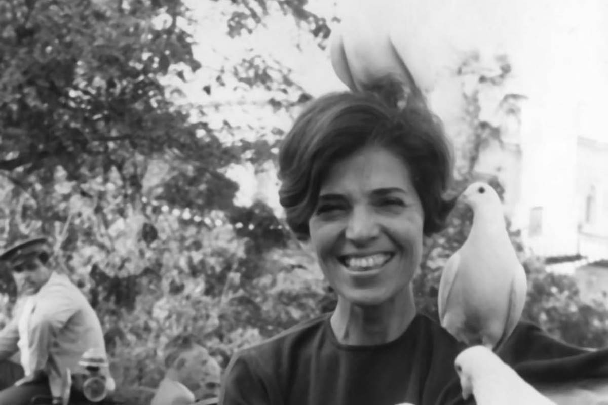 Imagem em preto e branco de Eunice Paiva sorrindo com pombas brancas ao redor - Metrópoles