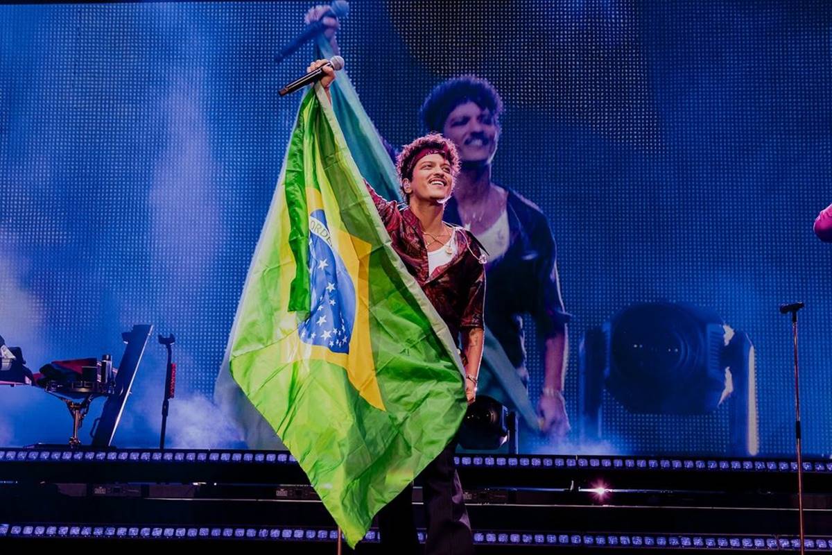 Bruno Mars segurando bandeira do Brasil durante show, enquanto sorri - Metrópoles