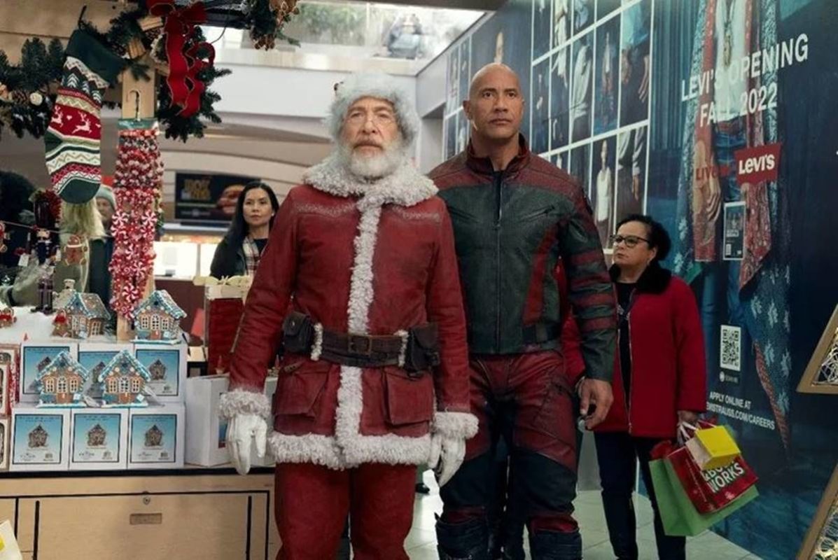 foto colorida de Dwayne Johnson e homem vestido de papai noel caminhando - metrópoles