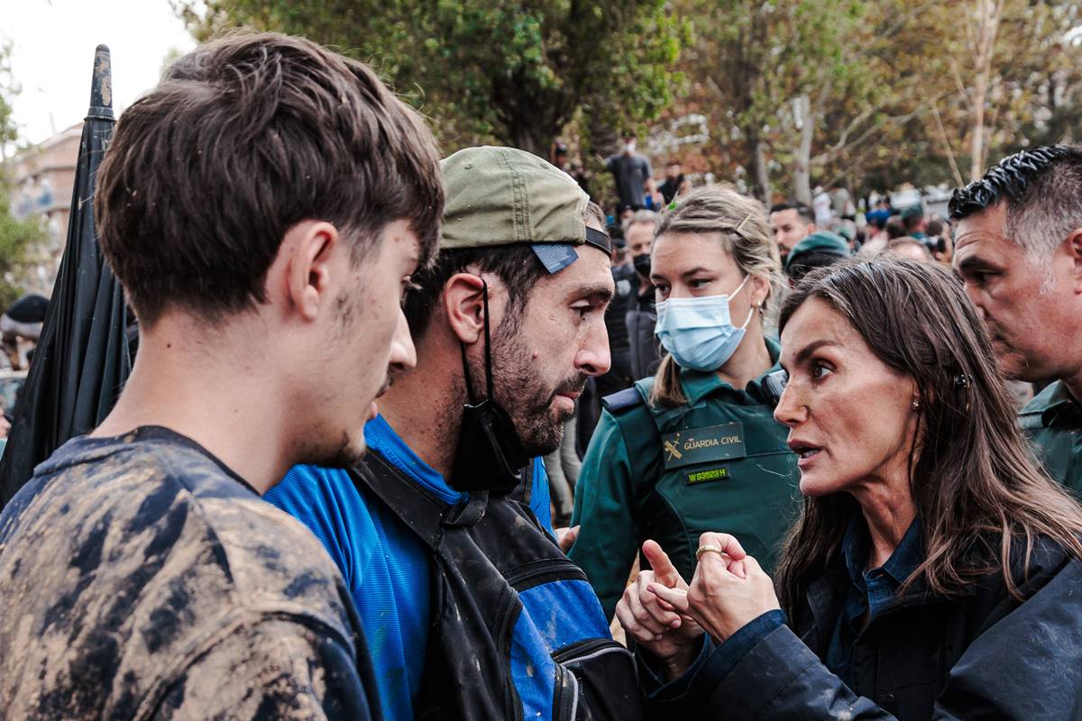 Foto colorida de mulher conversando com homens sujos de lama - Metrópoles