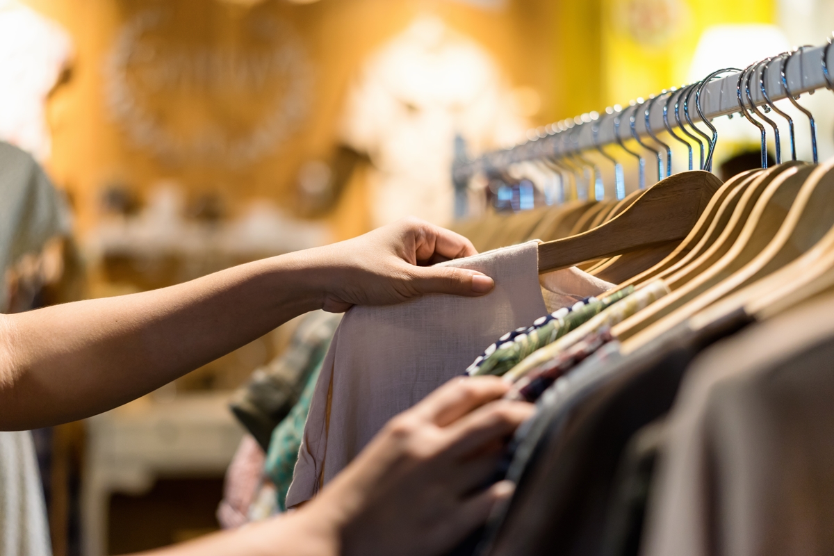 Imagem mostra mão de mulher tirando camisa que esté pendurada em um cabide de uma arara de roupas - Metrópoles