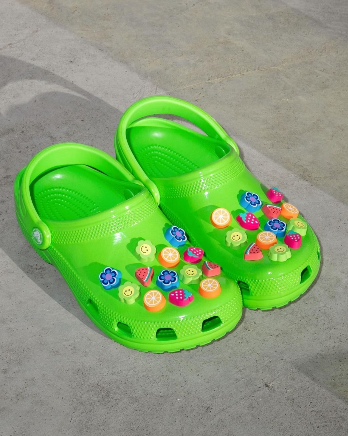 A imagem mostra uma Crocs verde com vários Jibbitz coloridos no calçado