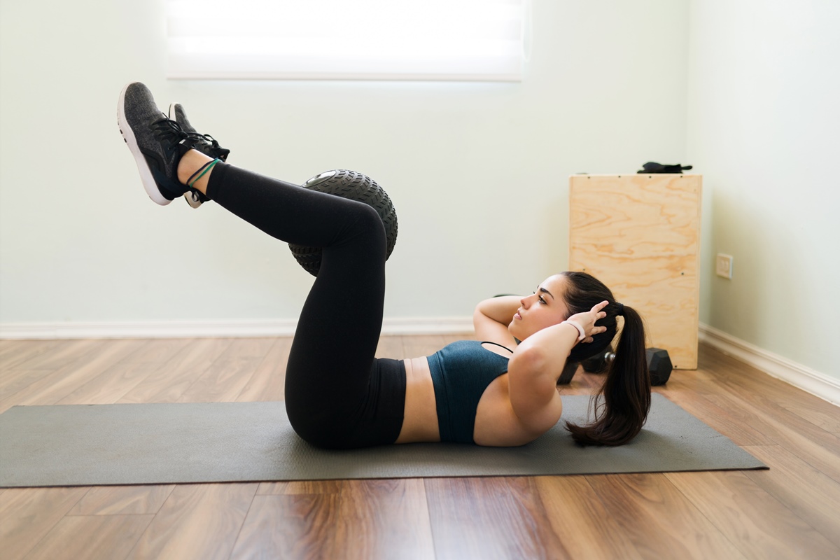 Vista lateral de uma jovem determinada segurando uma bola de slam com as pernas e fazendo abdominais para ter abdominais planos