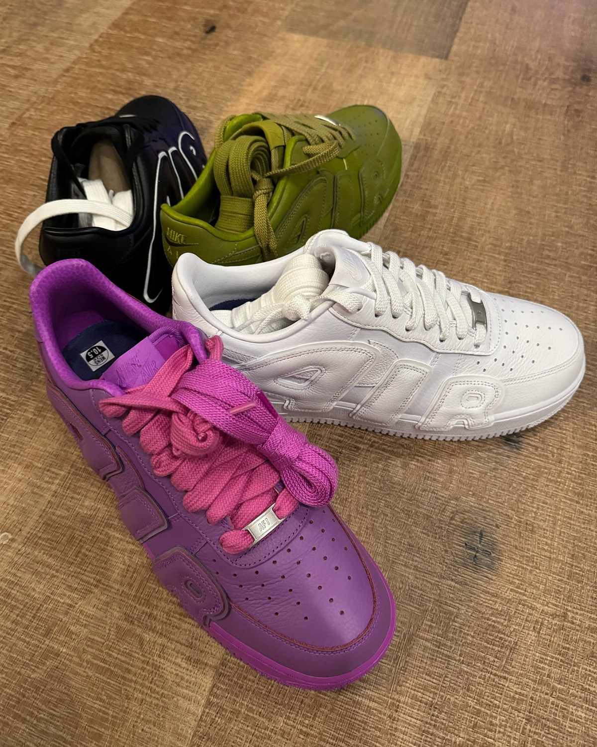 A imagem mostra quatro sneakers do mesmo modelo em cores diferentes. Um preto, branco, verde e um último em roxo