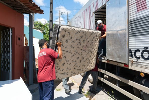 Foto colorida de 3 homens colocando um colchão no caminhão - Metrópoles 