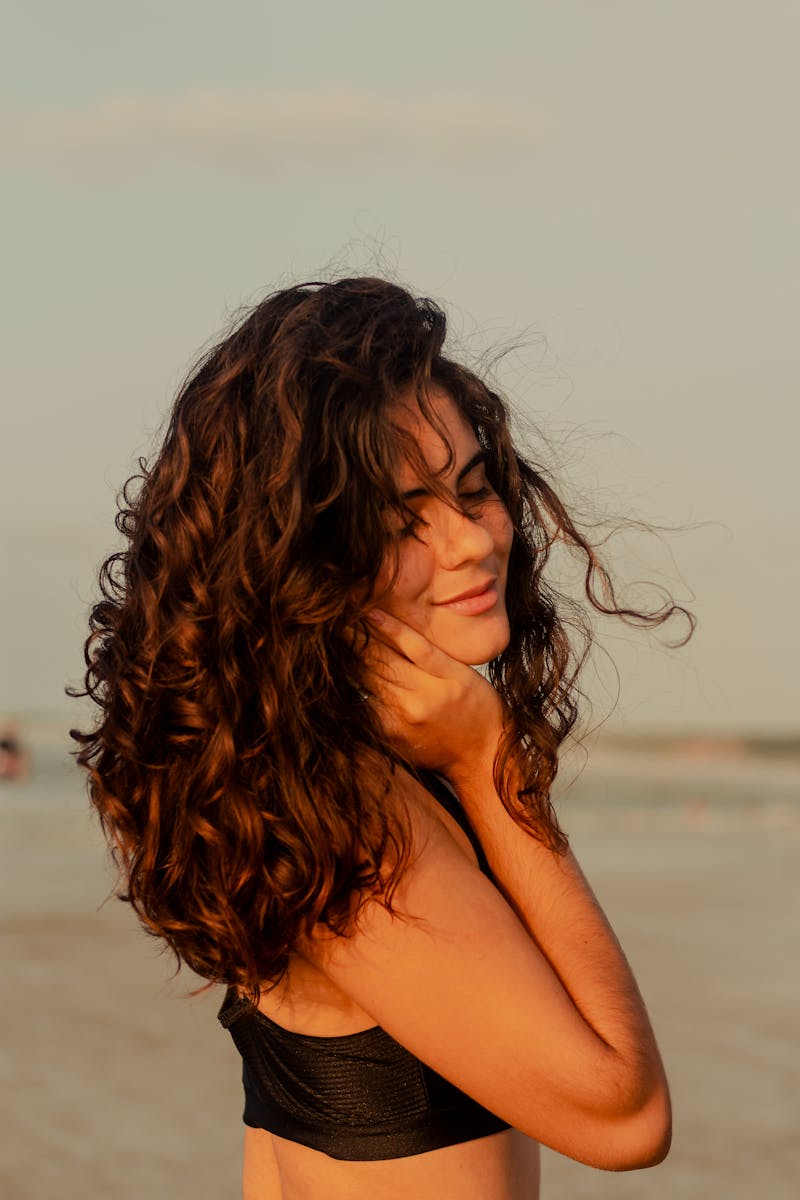 Jovem mulher de cabelo cacheado na praia com mar ao fundo - Metrópoles