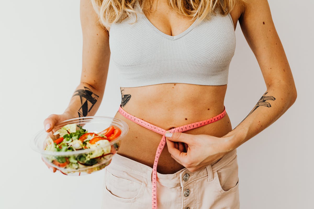 Mulher segurando porção de salada em uma mão e uma fita métrica ao redor da cintura - Metrópoles