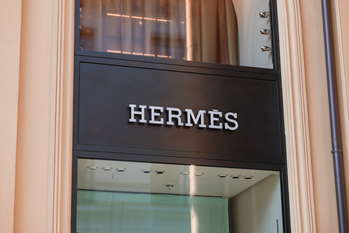 A imagem mostra a faixada da loja da Hermès na Alemanha. Em uma fundo preto, a tipografia da marca aparece em alto-relevo na entrada principal da loja.