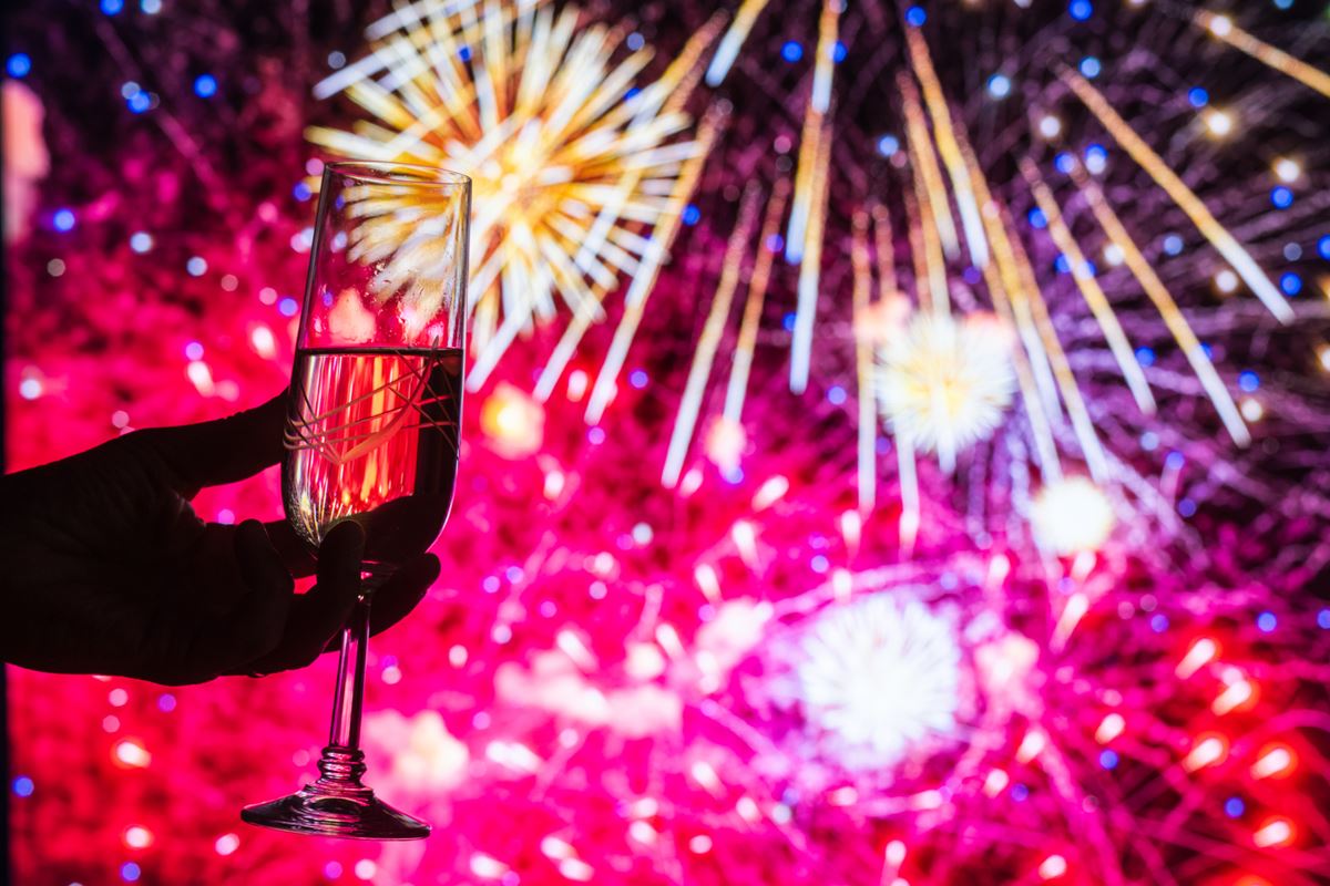 Foto colorida de taça de espumante e atrás fogos de artifícios - Metrópoles