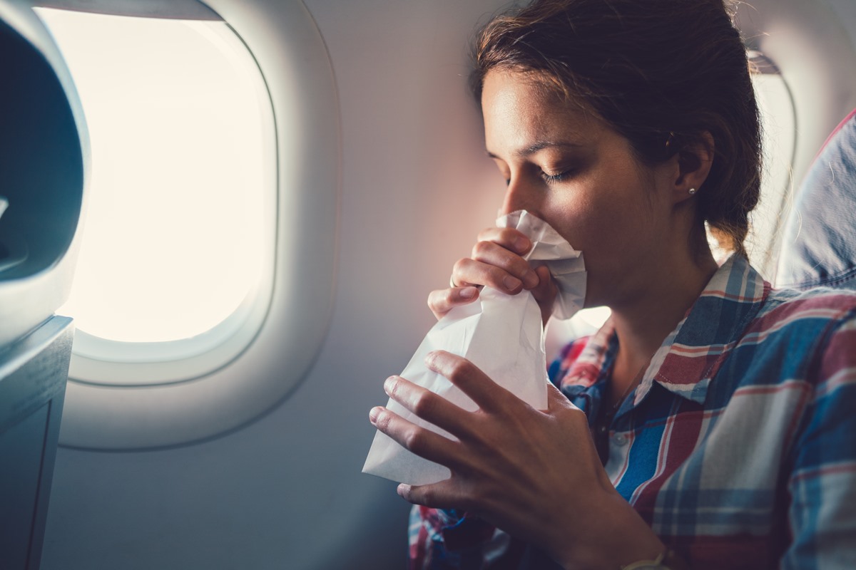 Foto colorida de mulher em avião vomitando dentro de saco de papel - Metrópoles