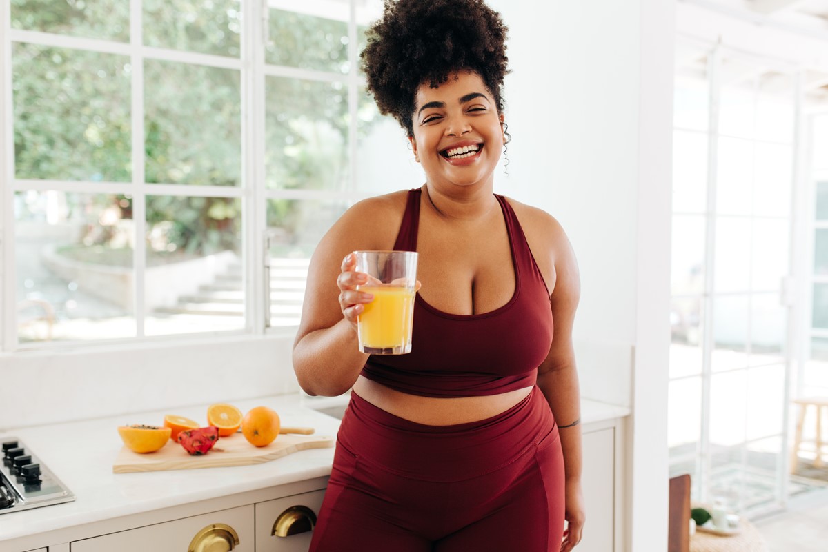 Foto colorida de mulher em cozinha segurando copo de suco - Metrópoles