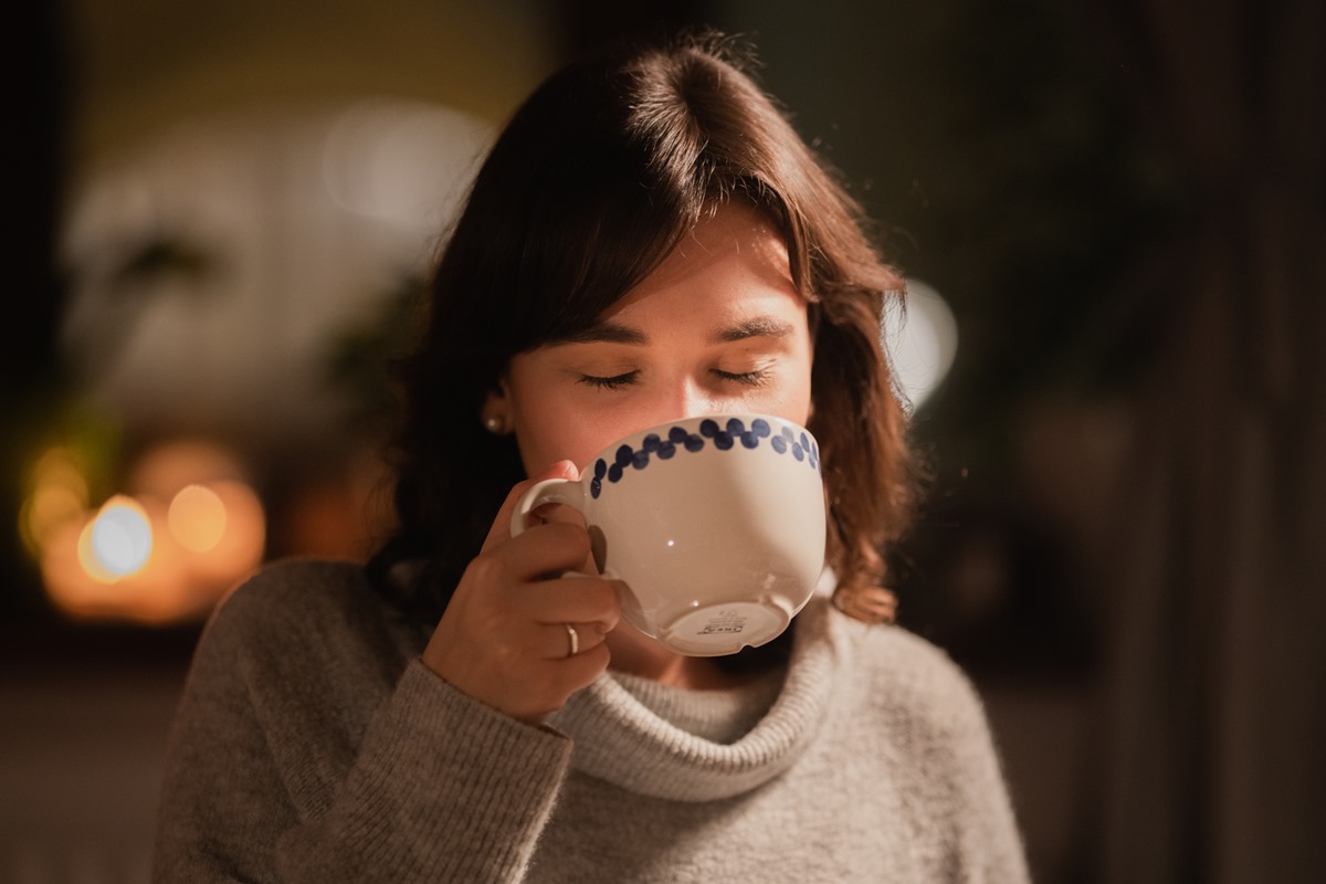 Foto colorida de mulher tomando café em um cenário noturno - Metrópoles