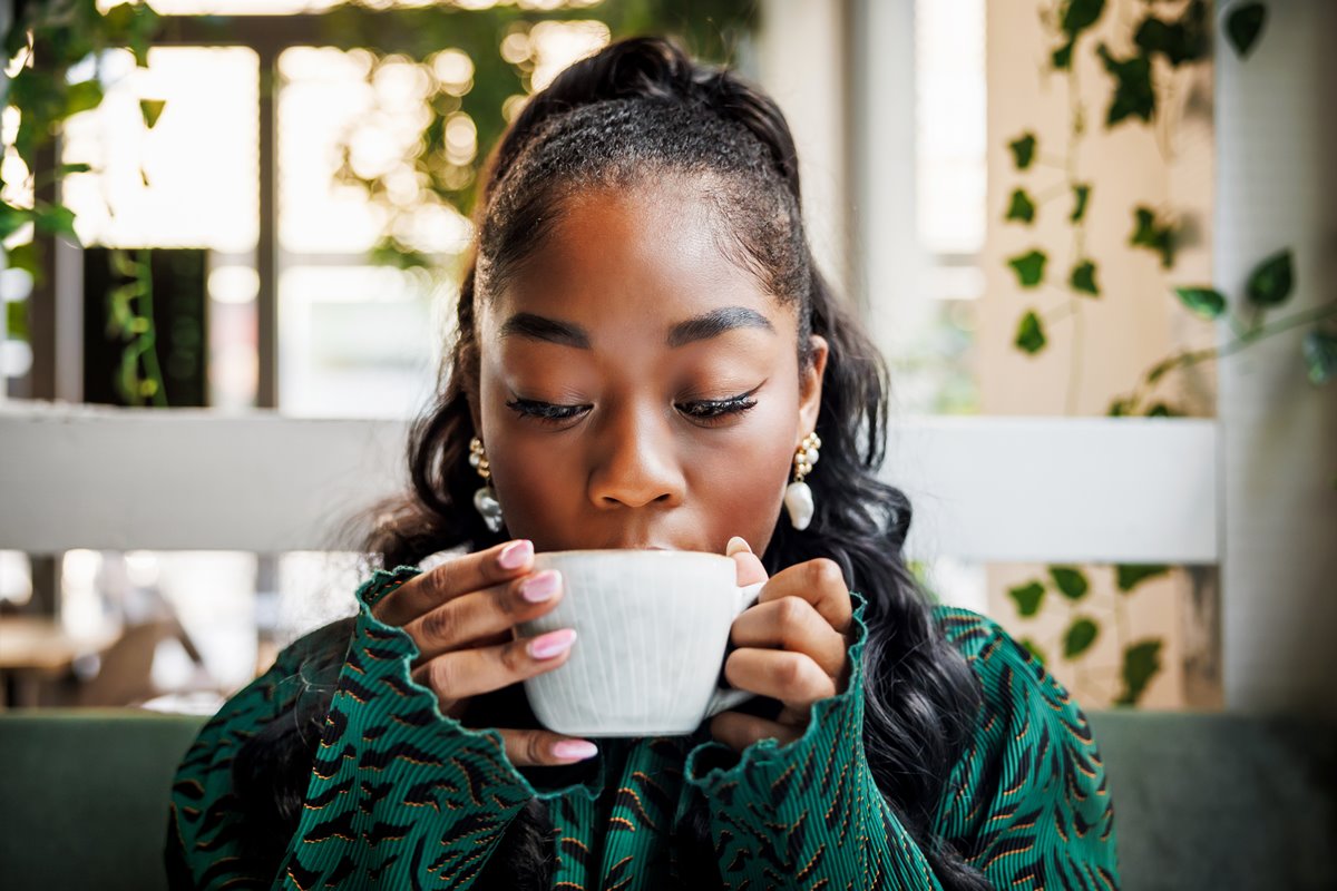 Foto colorida de mulher com xícara de café na boca - Metrópoles