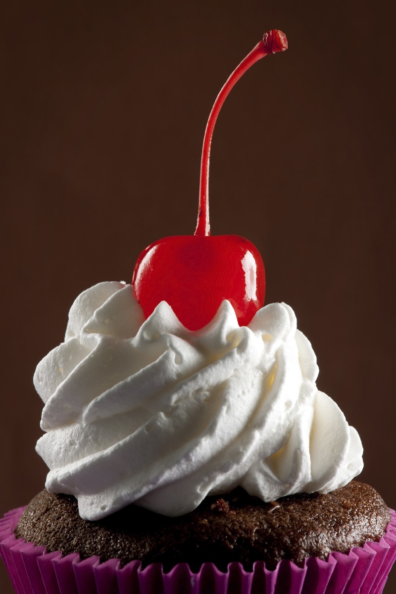 Foto colorida de cupacke com cereja e chantilly - Metrópoles