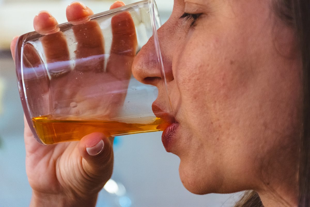 Foto colorida de mulher tomando bebida em copo de vidro transparente - Metrópoles