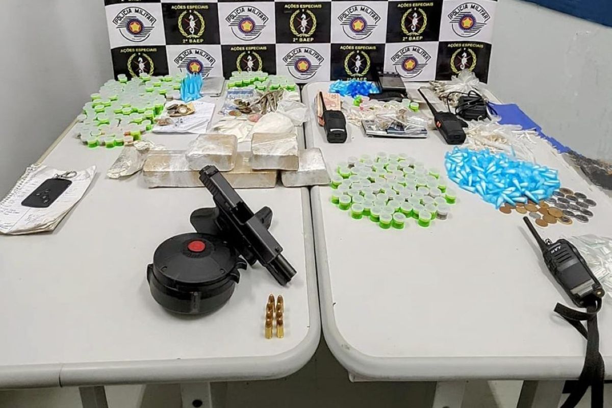 Imagem colorida de uma mesa com drogas, pistolas e balanças de precisão apreendidas pela PM - Metrópoles