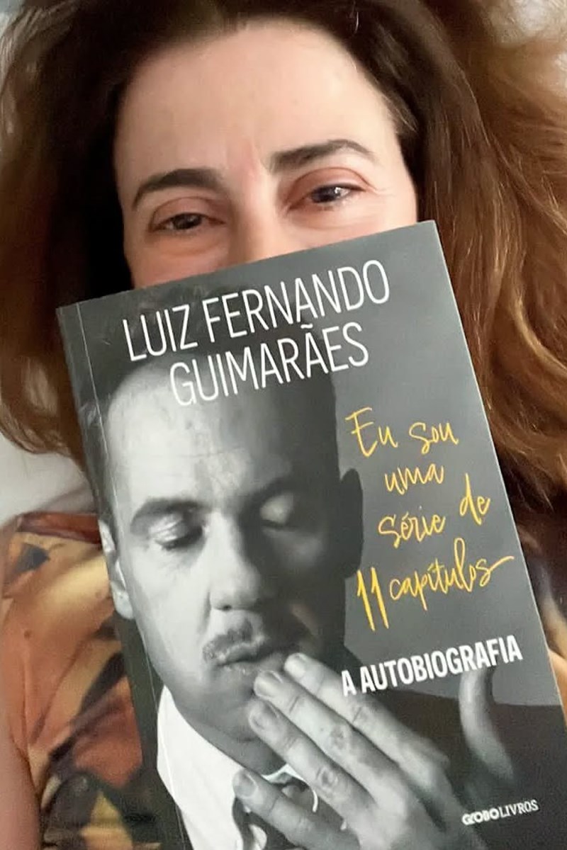 Foto colorida de mulher com livro em frente ao rosto - Metrópoles