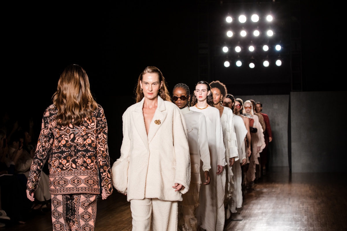 A imagem mostra modelos enfileirados andando na passarela do São Paulo Fashion Week