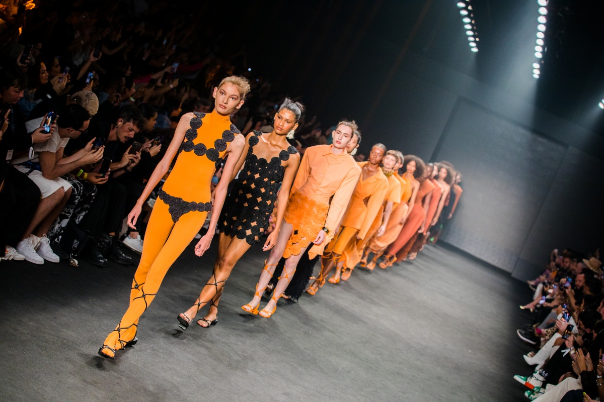 A imagem mostra modelos enfileirados andando na passarela do São Paulo Fashion Week