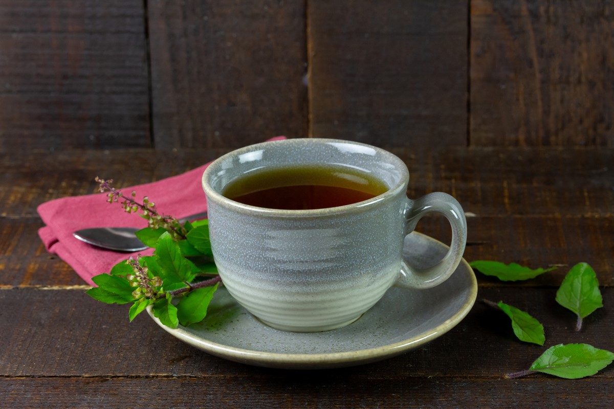 Chá de manjericão em xícara cinza com folha de tulsi fresca em fundo de madeira. Metrópoles