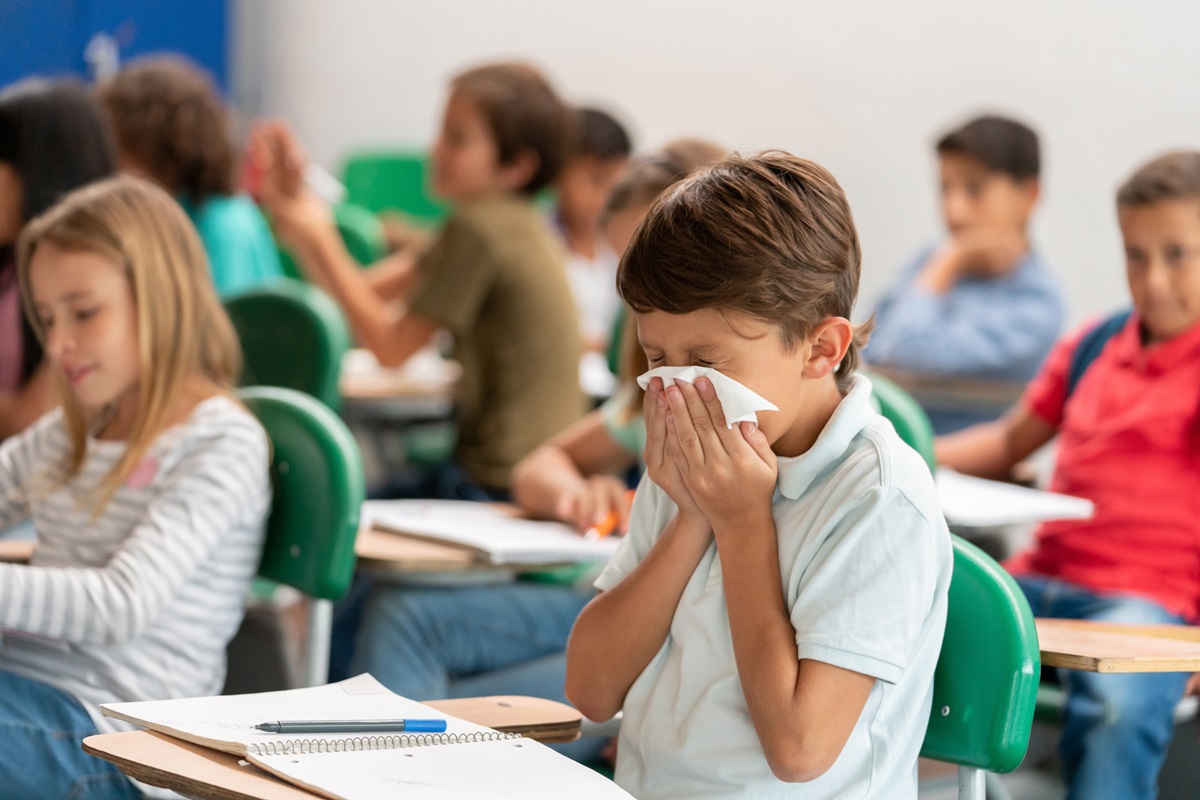 Retrato de um menino doente na escola assoando o nariz na aula - conceitos de estilo de vida