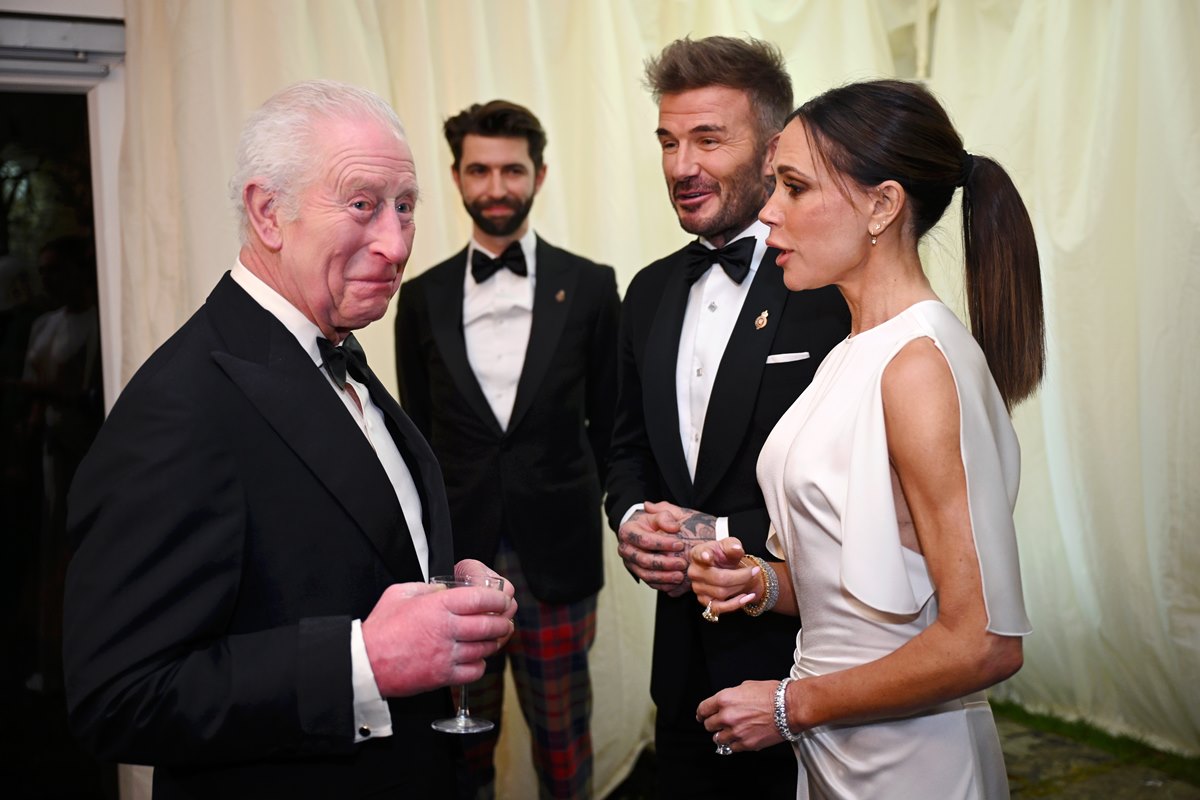 Foto colorida de três homens de terno conversando com uma mulher, com vestido branco. Eles estão com taças na mão - Metrópoles