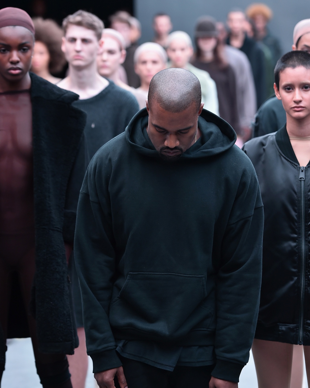 A imagem mostra o artista Kanye West em frente diversos modelos