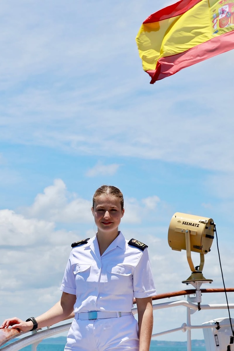 Foto colorida de mulher em embarcação. Ao fundo, aparece a bandeira da Espanha - Metrópoles