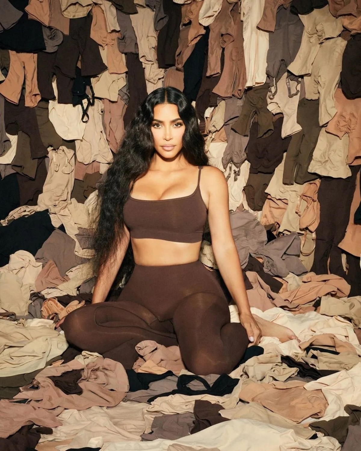 A imagem mostra Kim Kardashian rodeada por roupas da sua linha Skims