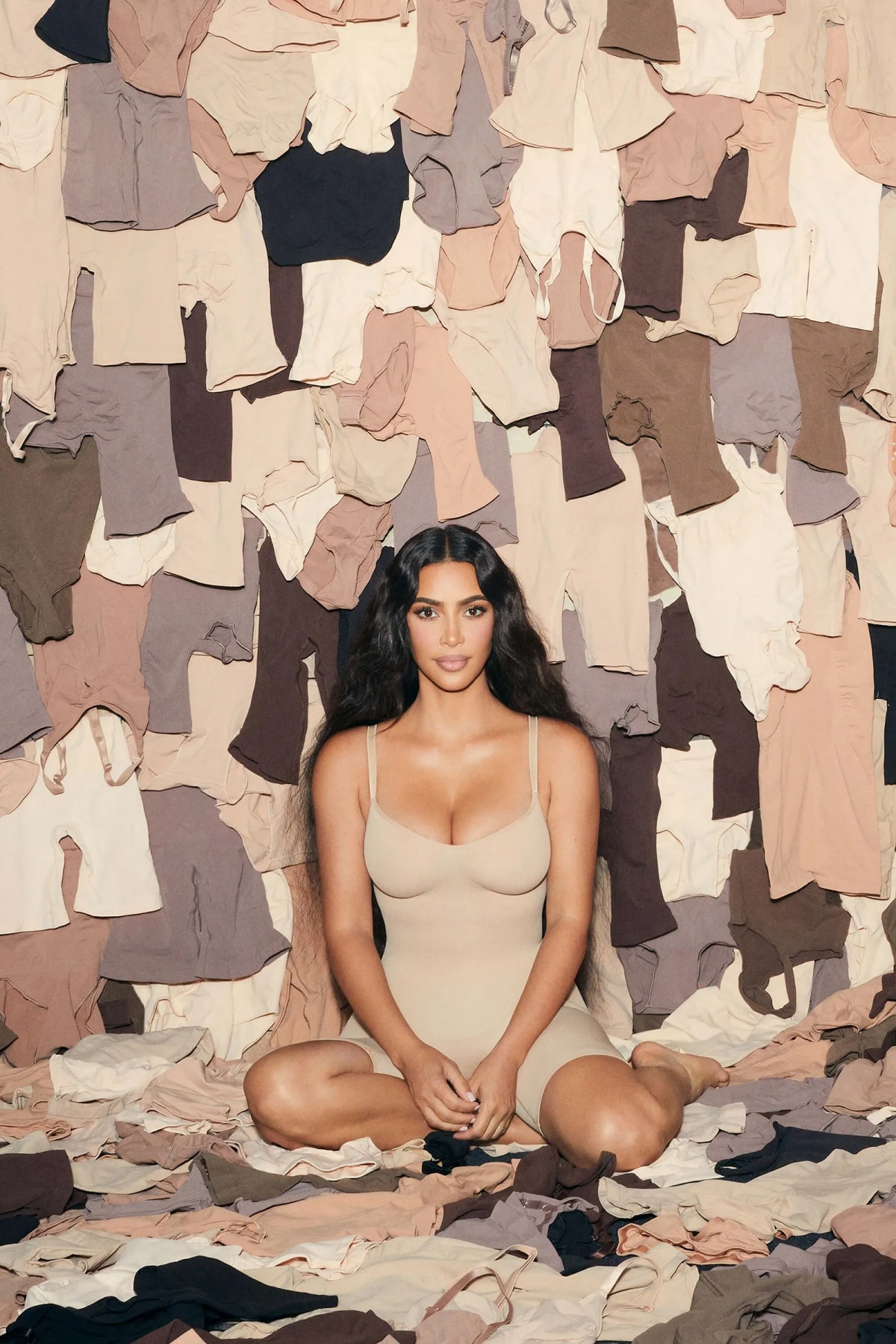 A imagem mostra Kim Kardashian rodeada por roupas da sua linha Skims