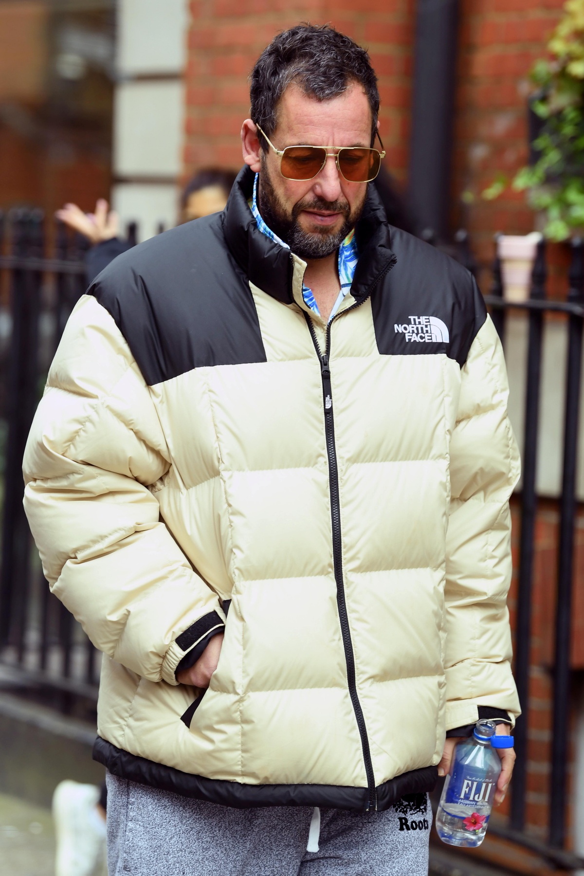 A imagem mostra o ator Adam Sandler vestindo um casaco da marca The North Face