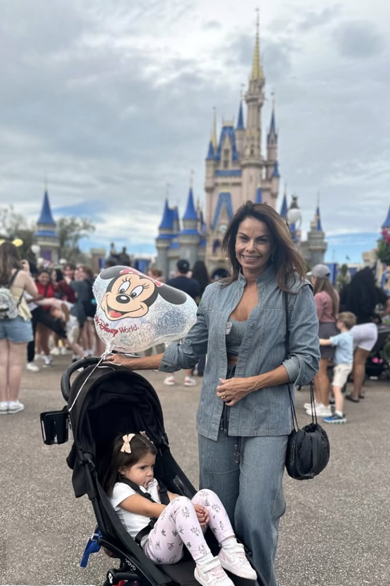 Foto colorida de mulher tirando foto em frente a um castelo da Disney. Uma menina em um carrinho de bebê aparece também - Metrópoles