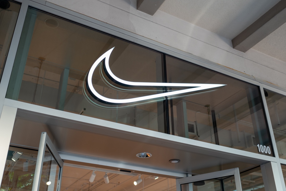 A imagem mostra a entrada de uma loja da Nike com o logo swoosh em led branco