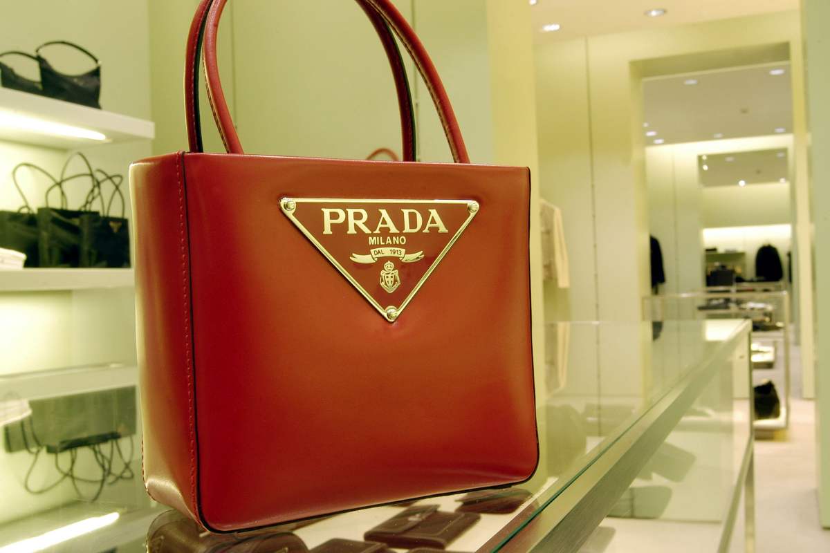 A imagem mostra uma bolsa da Prada vermelha em cima de uma bancada de uma loja com outros produtos ao fundo