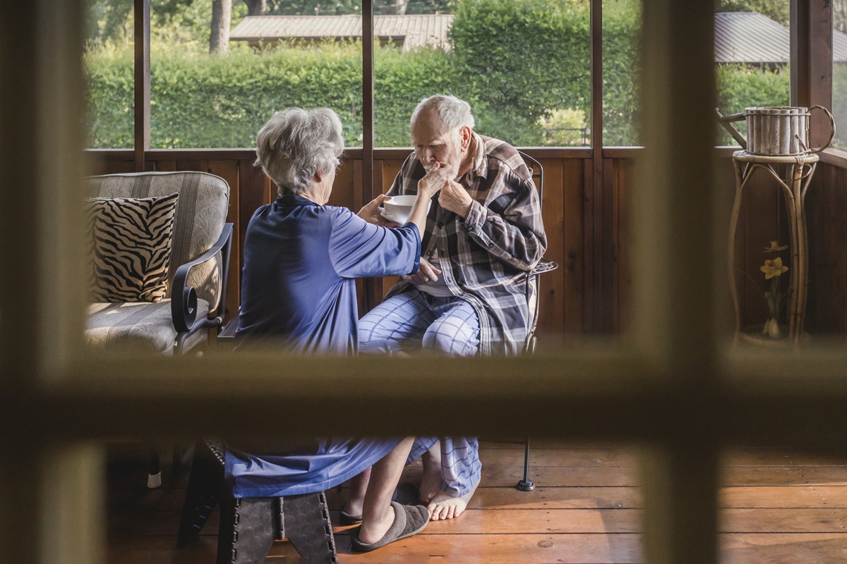 Cuidadora alimenta idoso frágil na varanda com tela - alzheimer - parkinson