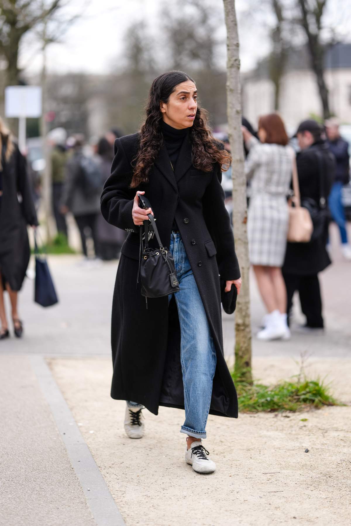 A imagem mostra uma mulher de casaco sobretudo e calça jeans enquanto caminha