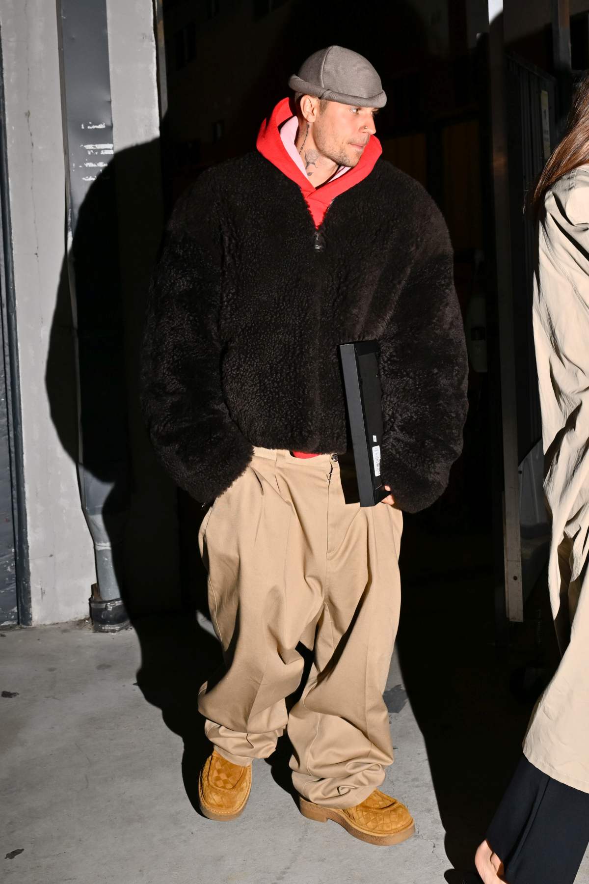 A imagem mostra o cantor Justin Bieber caminhando vestindo um casaco preto grosso e uma calça caqui