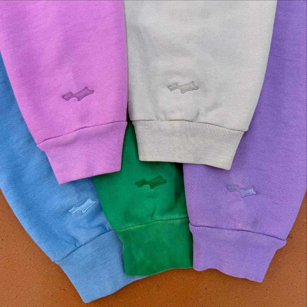 A imagem mostra cinco mangas de casaco moletom, nas cores azul, verde, roxo, rosa, lilás e branco