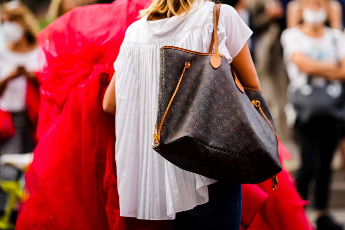 A imagem mostra uma mulher de camisa branca carregando uma bolsa da Louis Vuitton
