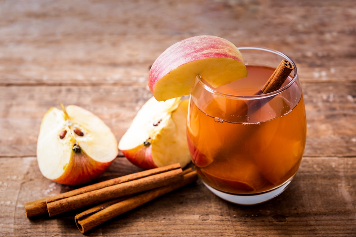 Imagem mostra copo de vidro cheio de chá de maçã, com pedaços da fruta e alguns paus de canela - Metrópoles