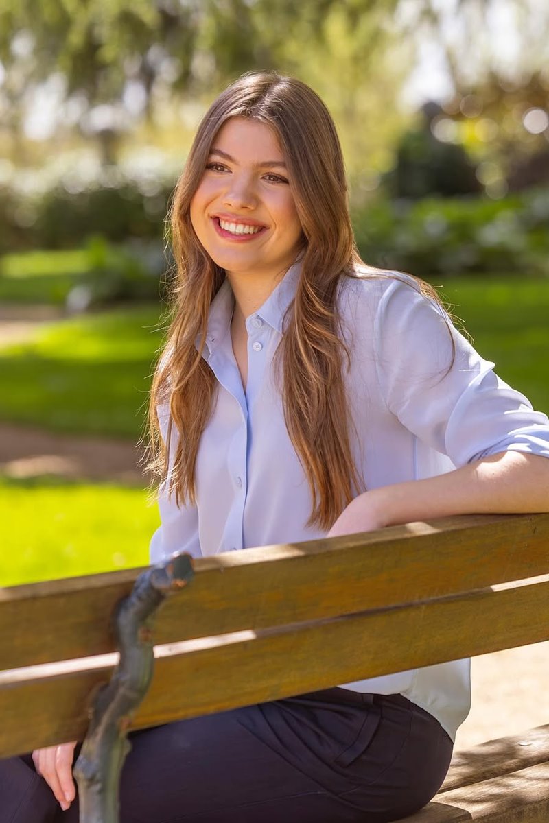 Foto colorida de mulher com cabelo longo. Ela está sorridente e próximo a um jardim - Metrópoles
