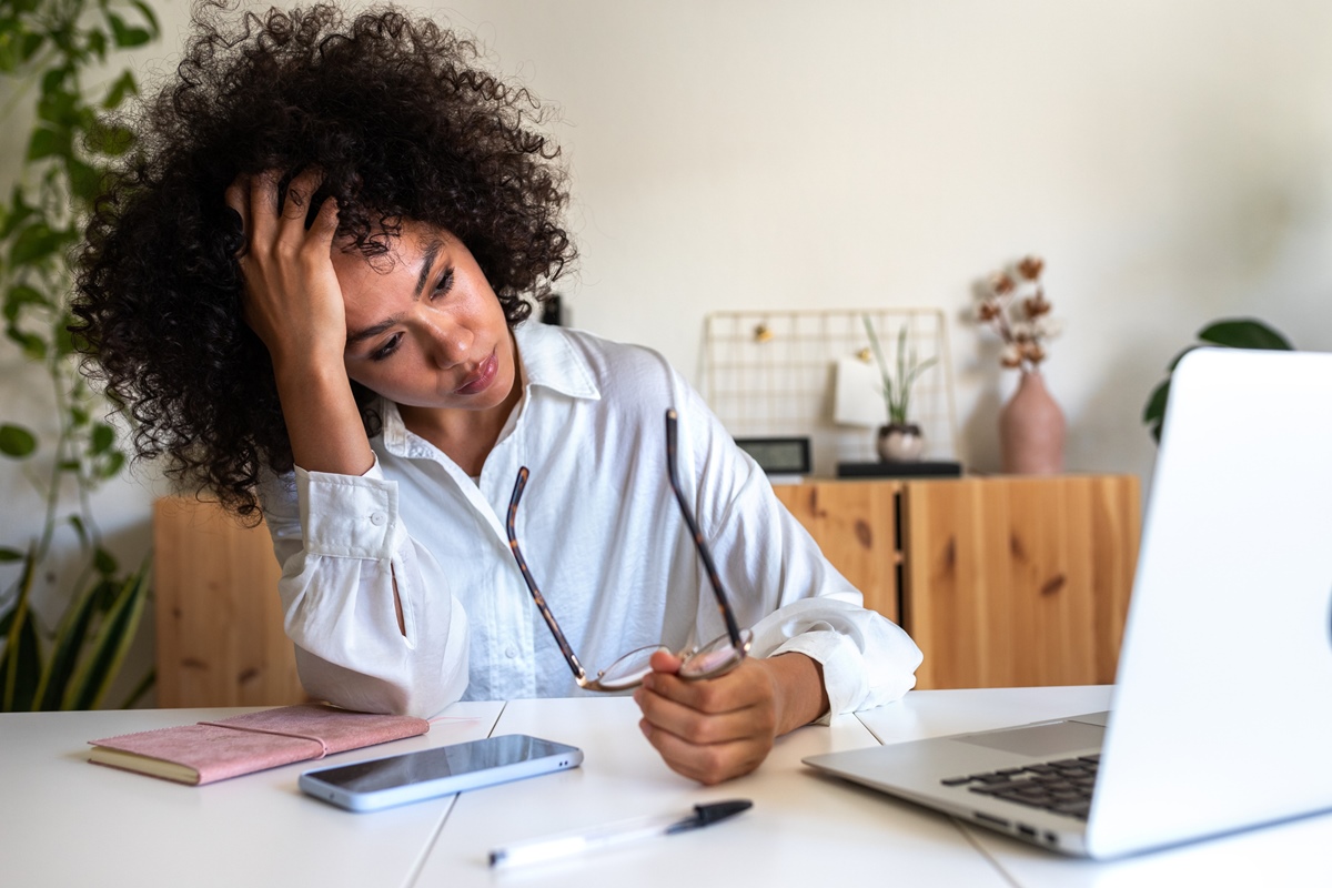 Jovem afro-americana sentindo-se exausta e deprimida sentada em frente ao laptop. Síndrome de burnout no trabalho. Conceito de saúde mental. Metrópoles