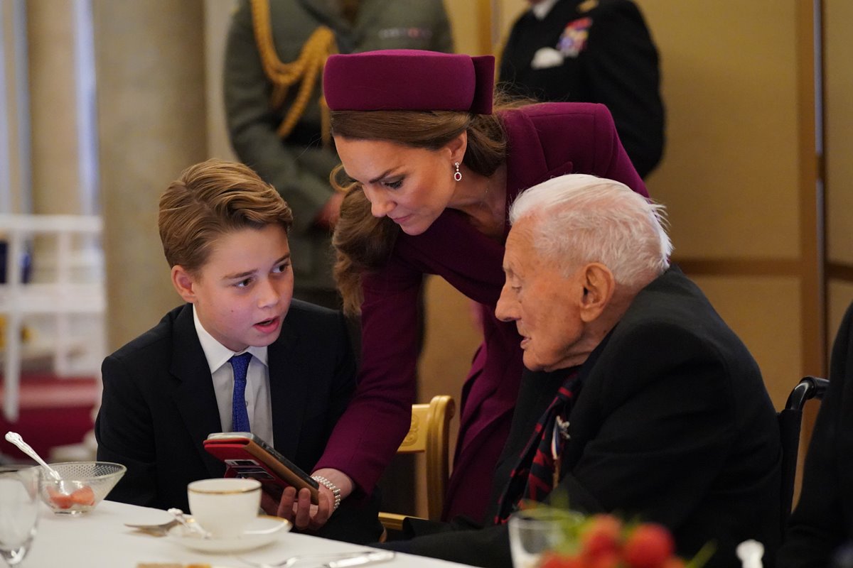 Foto colorida de menino conversando com homem ao lado, enquanto mulher mostra algo em telefone - Metrópoles
