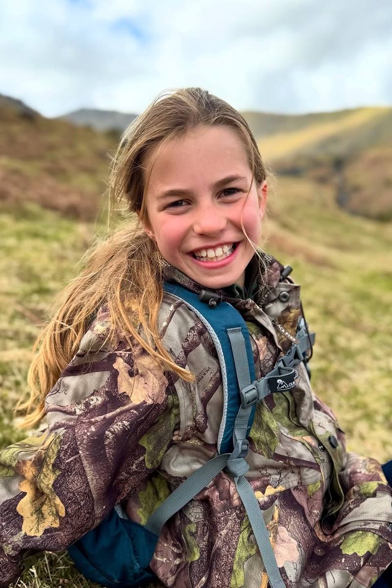 Foto colorida de menina com casaco estampado e cabelo preso. Ela está sorridente - Metrópoles