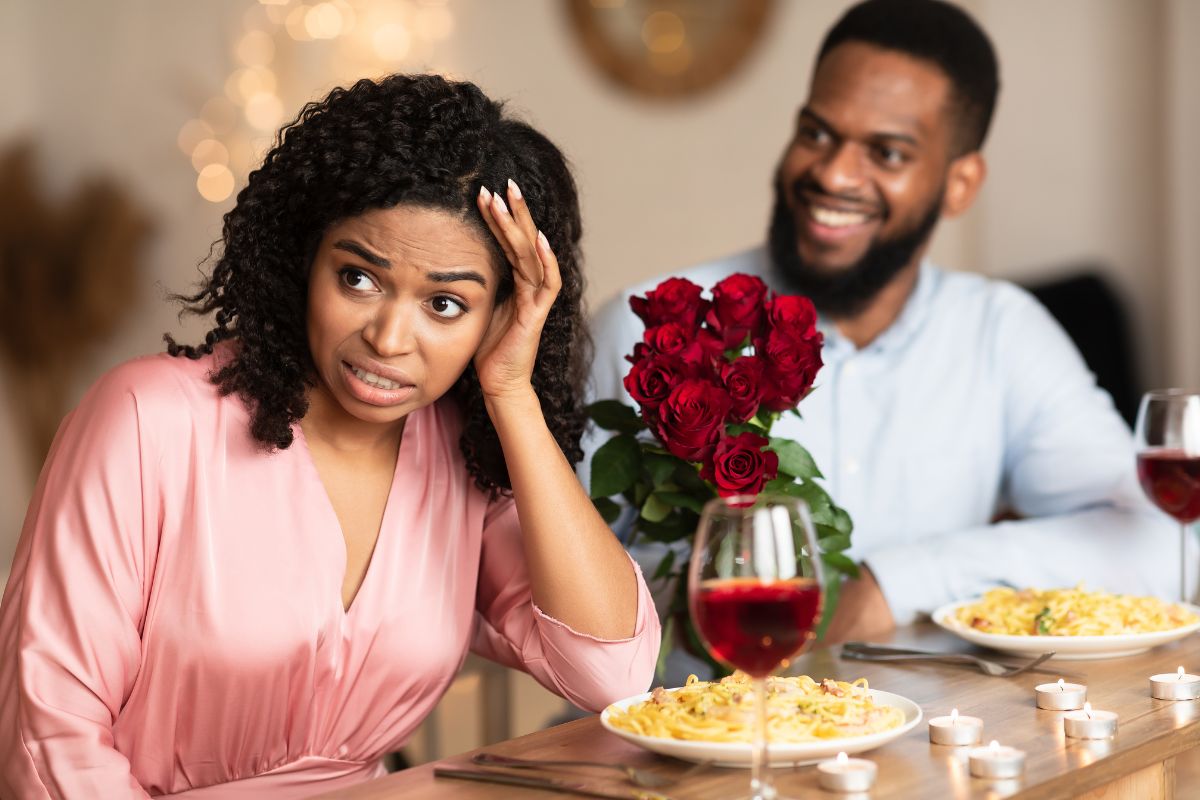 Foto colorida de um casal negro em um jantar romântico a mulher está claramente incomodada com o encontro