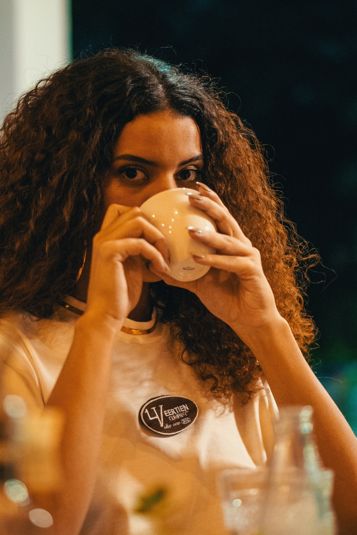 A imagem mostra uma jovem tomando café usando uma camiseta branca