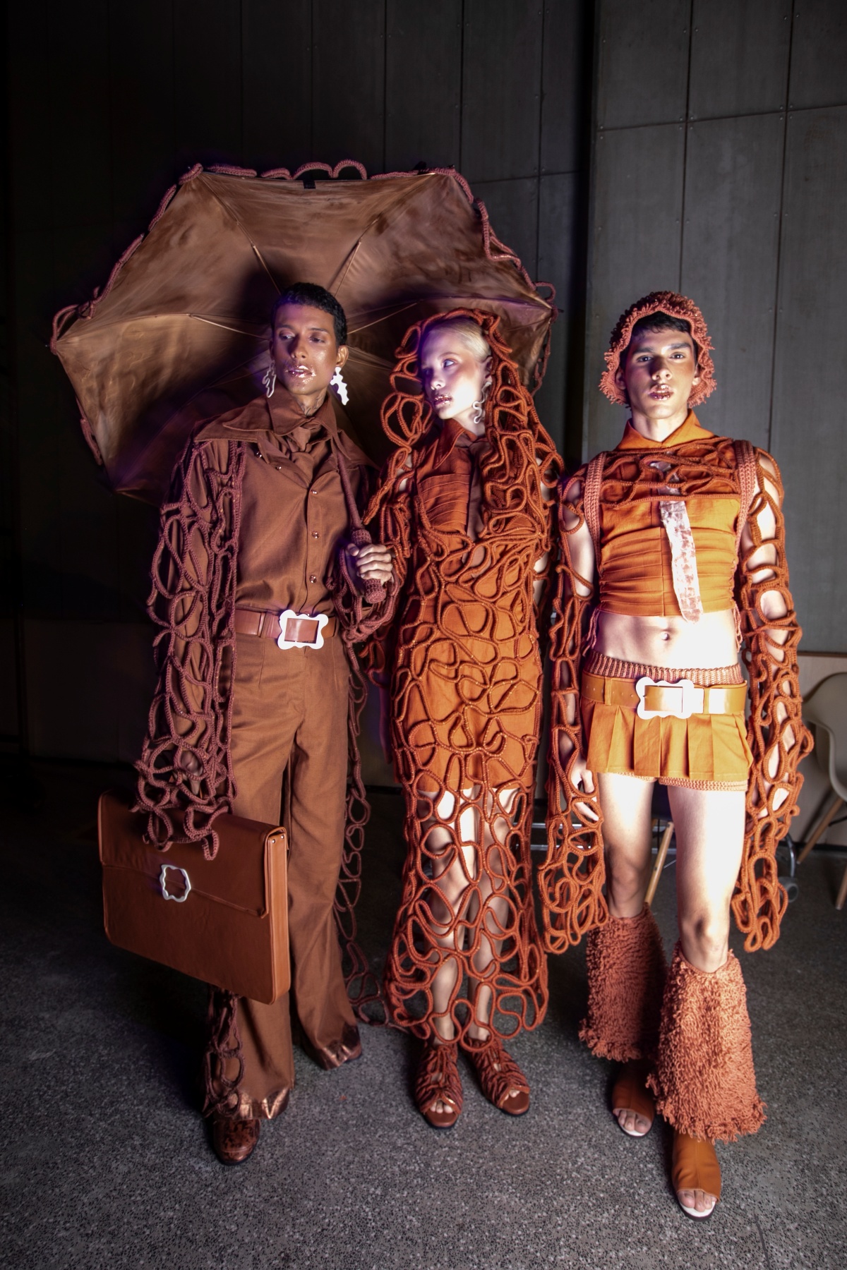 A imagem mostra três modelos posando com roupas rústicas em tons terrosos